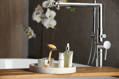 Photo of Bath tray with natural face roller and cosmetic products on tub