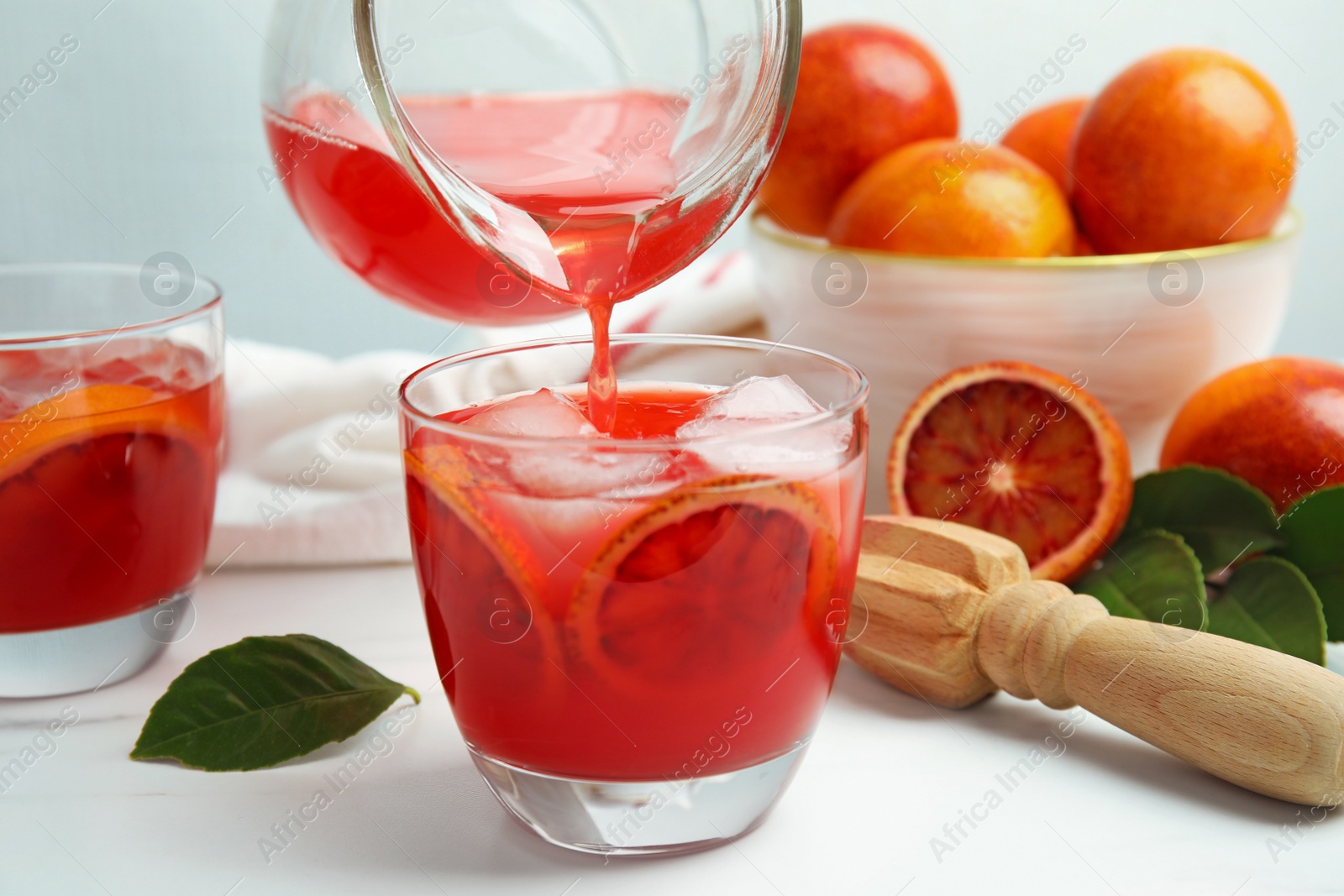 Photo of Pouring tasty sicilian orange juice into glass on white table