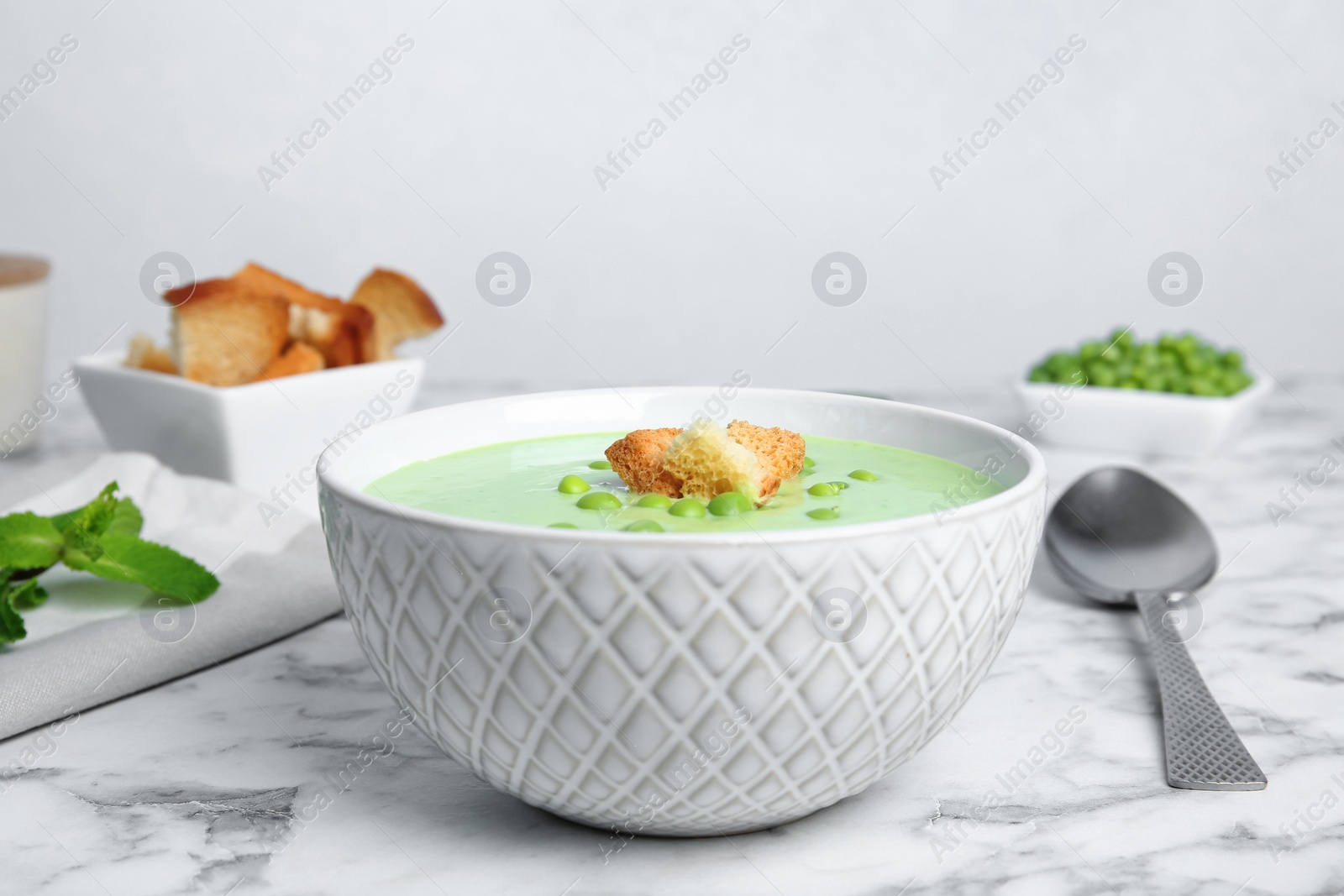 Photo of Green pea soup with croutons in bowl on table