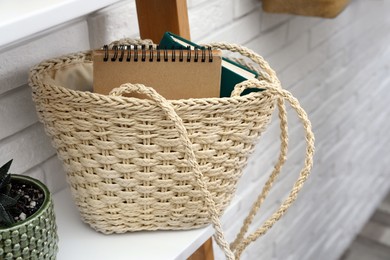 Stylish beach bag with notebooks on shelf indoors