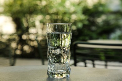 Glass of fresh water on grey table outdoors