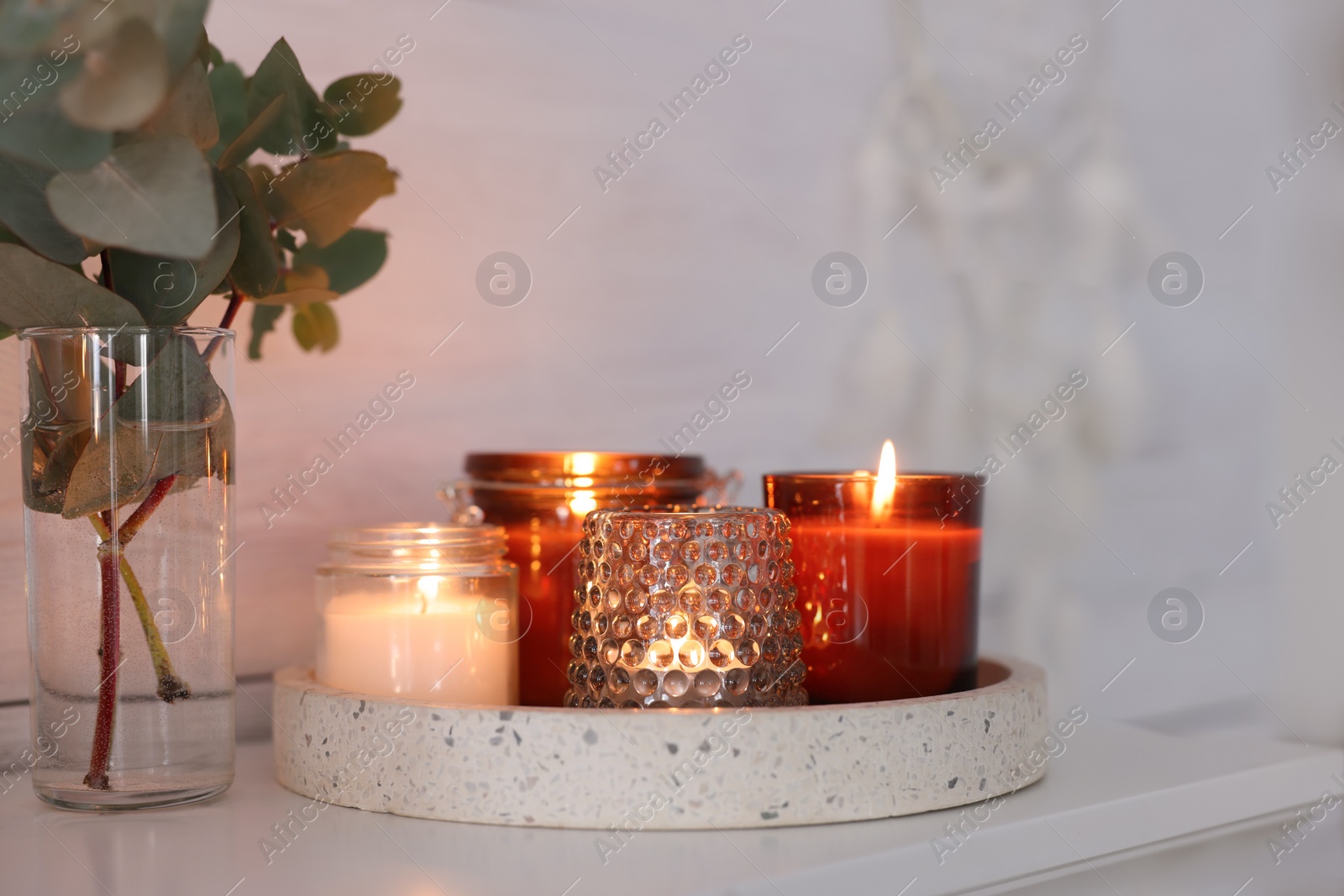 Photo of Burning candles on mantel near white wall indoors