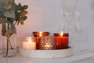 Burning candles on mantel near white wall indoors