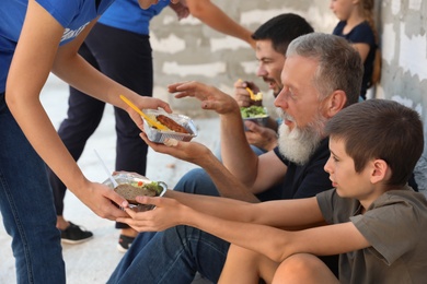Photo of Poor people receiving food from volunteers near wall outdoors