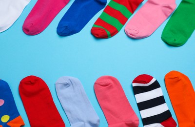 Photo of Many different colorful socks on light blue background, flat lay