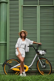 Beautiful young woman with bicycle near green wall outdoors