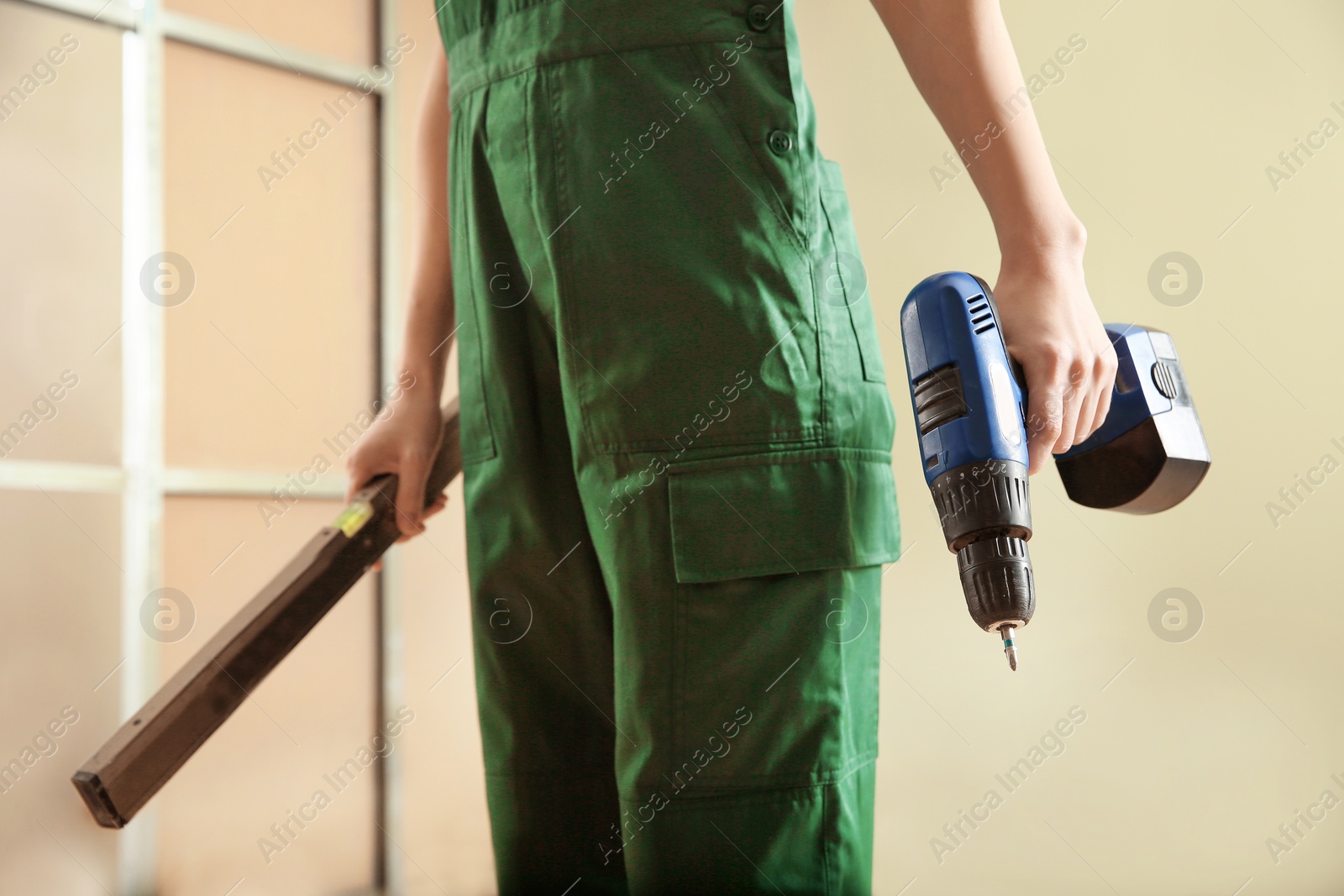 Photo of Professional builder with drill and level indoors, closeup. Home repair service