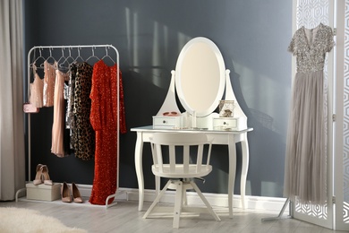 Photo of Rack with collection of beautiful festive clothes and dressing table in stylish room interior