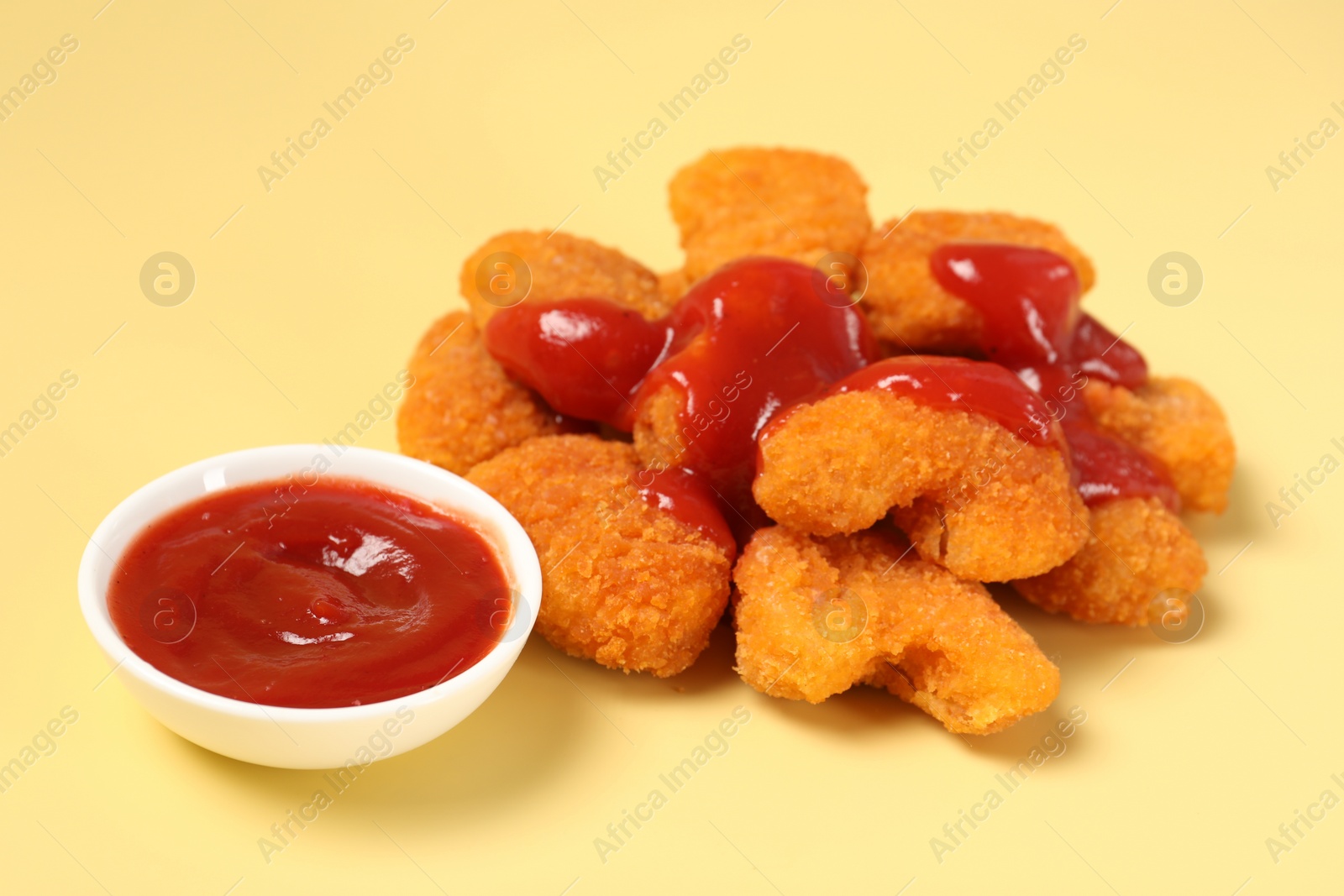 Photo of Tasty chicken nuggets with ketchup on pale yellow background