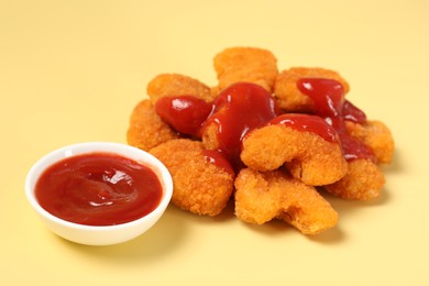 Tasty chicken nuggets with ketchup on pale yellow background