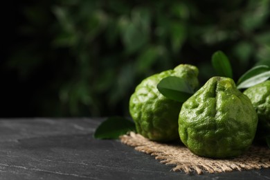 Photo of Fresh ripe bergamot fruits with green leaves on black table against blurred background, space for text