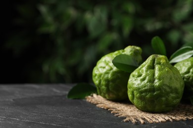 Fresh ripe bergamot fruits with green leaves on black table against blurred background, space for text