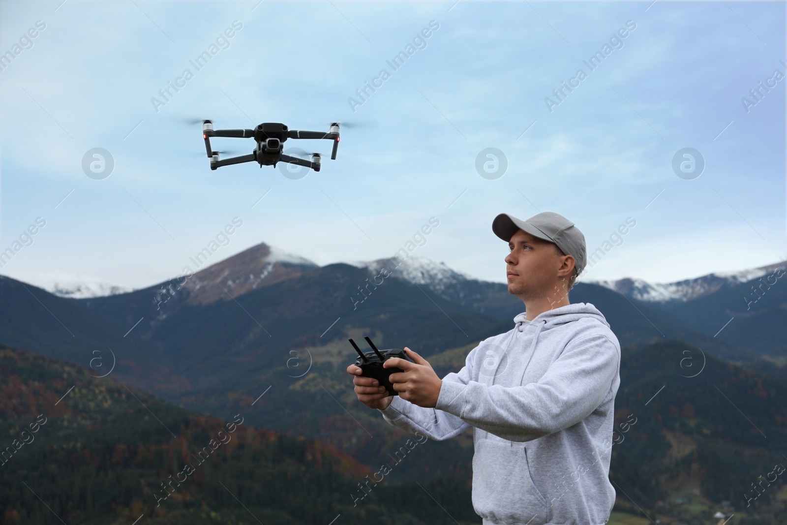 Photo of Young man operating modern drone with remote control in mountains