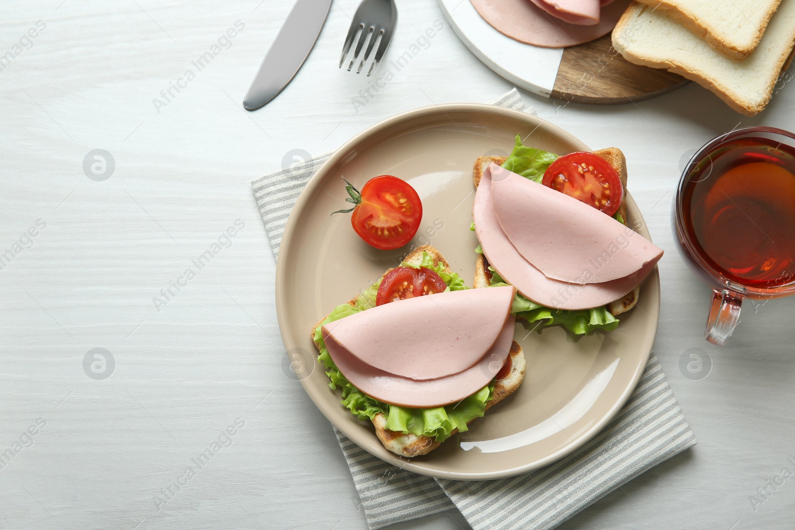 Photo of Plate of tasty sandwiches with boiled sausage, tomato and lettuce on white wooden table, flat lay. Space for text