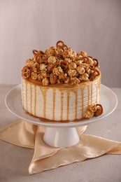 Photo of Caramel drip cake decorated with popcorn and pretzels on light grey table