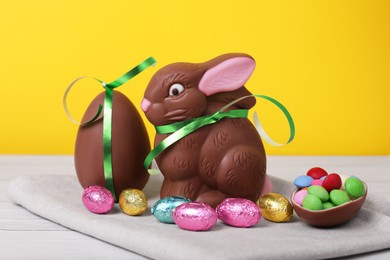 Photo of Chocolate Easter bunny, eggs and candies on white wooden table against yellow background, closeup