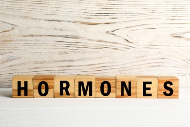 Photo of Word Hormones made of wooden cubes with letters on white table, space for text