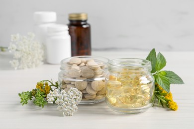 Photo of Jars with different pills, flowers and herbs on white wooden table. Dietary supplements