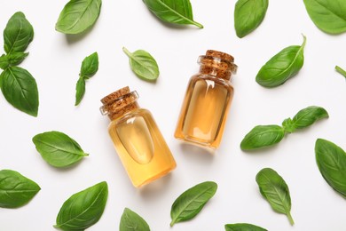 Photo of Bottles of essential basil oil and fresh leaves on white background, flat lay