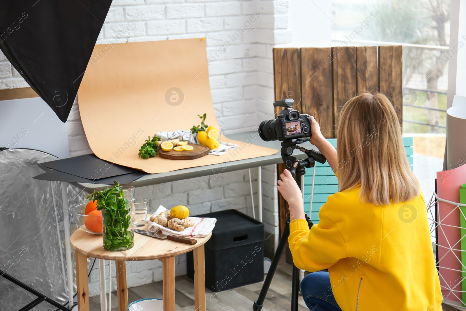 Photo of Young woman taking picture of lemons, mint and ginger in professional studio. Food photography