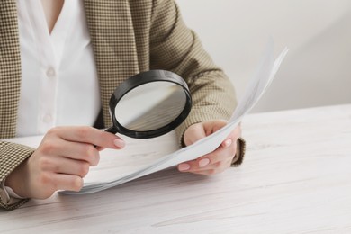 Photo of Woman looking at document through magnifier at wooden table, closeup. Searching concept