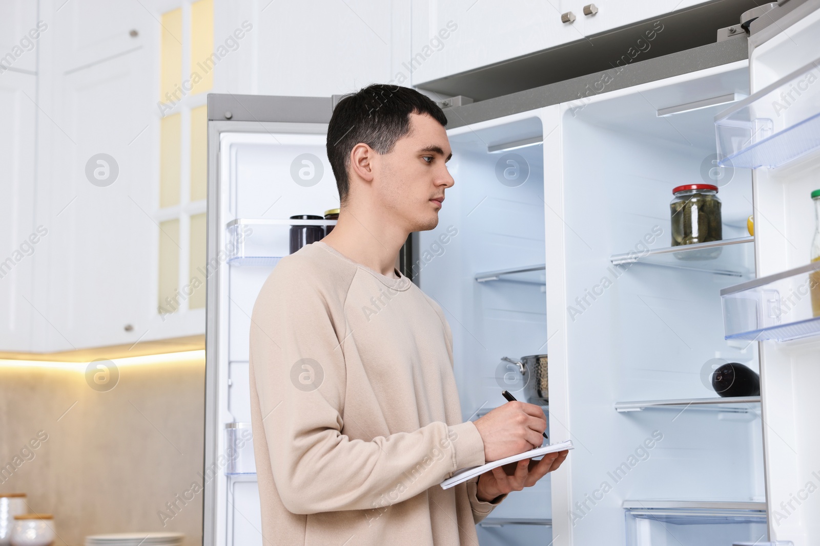 Photo of Man writing notes near empty refrigerator in kitchen