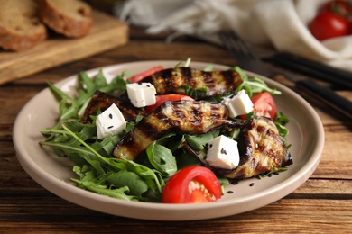 Photo of Delicious salad with roasted eggplant, feta cheese and arugula served on wooden table, closeup