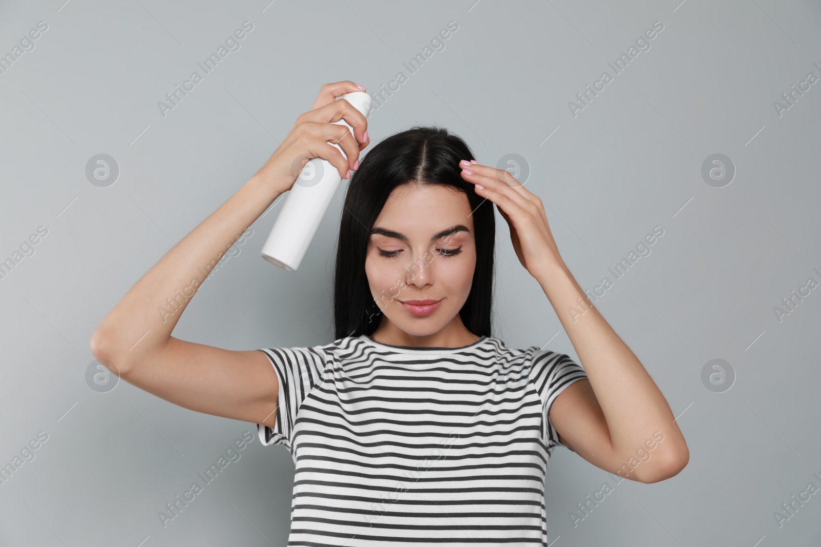 Photo of Woman applying dry shampoo onto her hair on light grey background