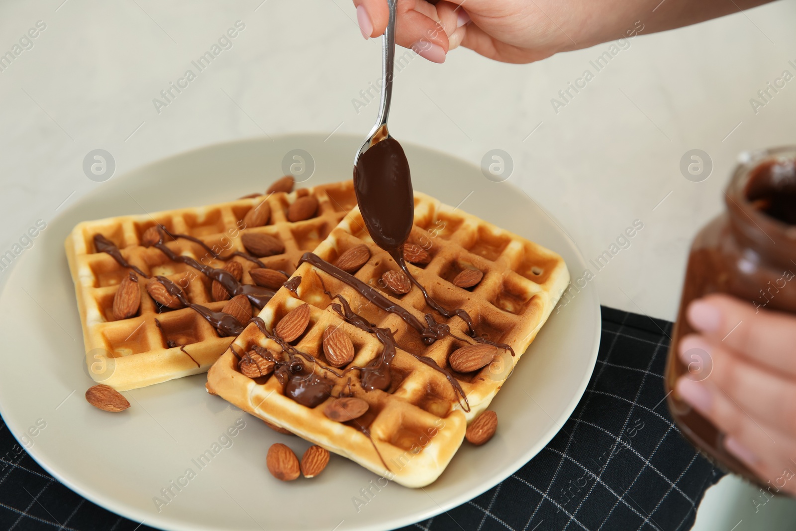 Photo of Woman decorating delicious Belgian waffles with chocolate cream at white table, closeup