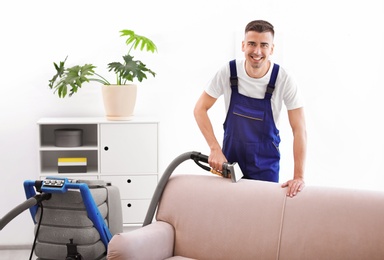 Dry cleaning worker removing dirt from sofa indoors