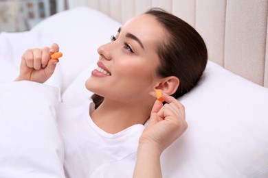Photo of Young woman inserting foam ear plugs in bed