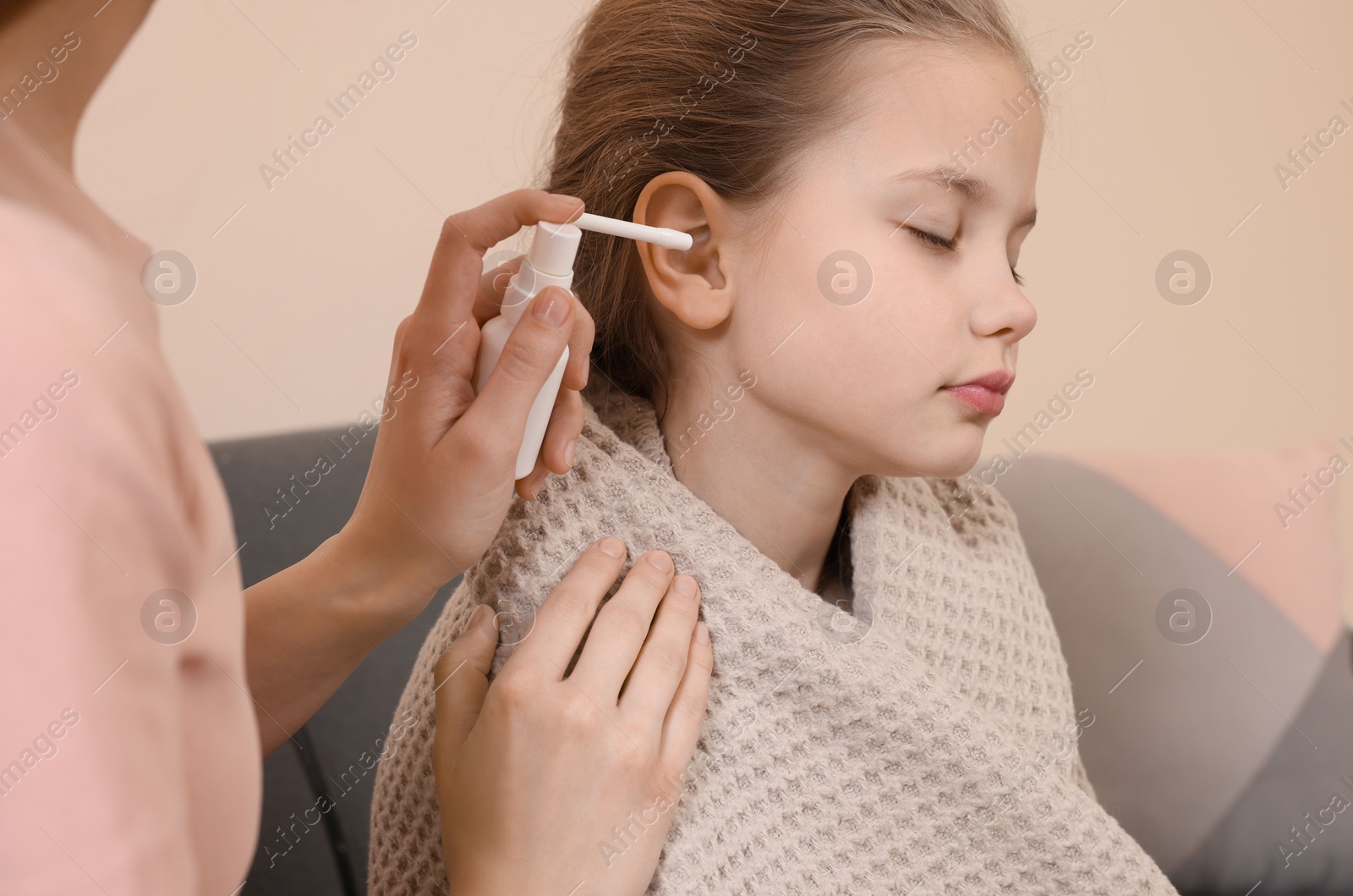 Photo of Mother spraying medication into daughter's ear in living room