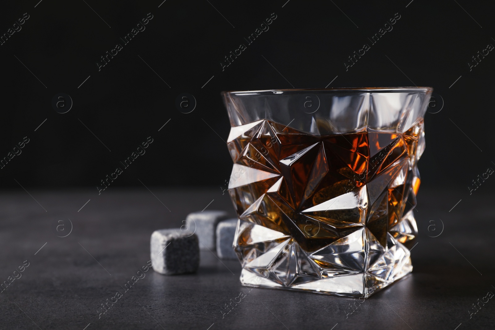 Photo of Golden whiskey in glass with cooling stones on table. Space for text