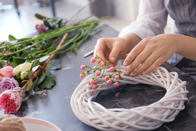 Female florist creating beautiful wreath at table, closeup