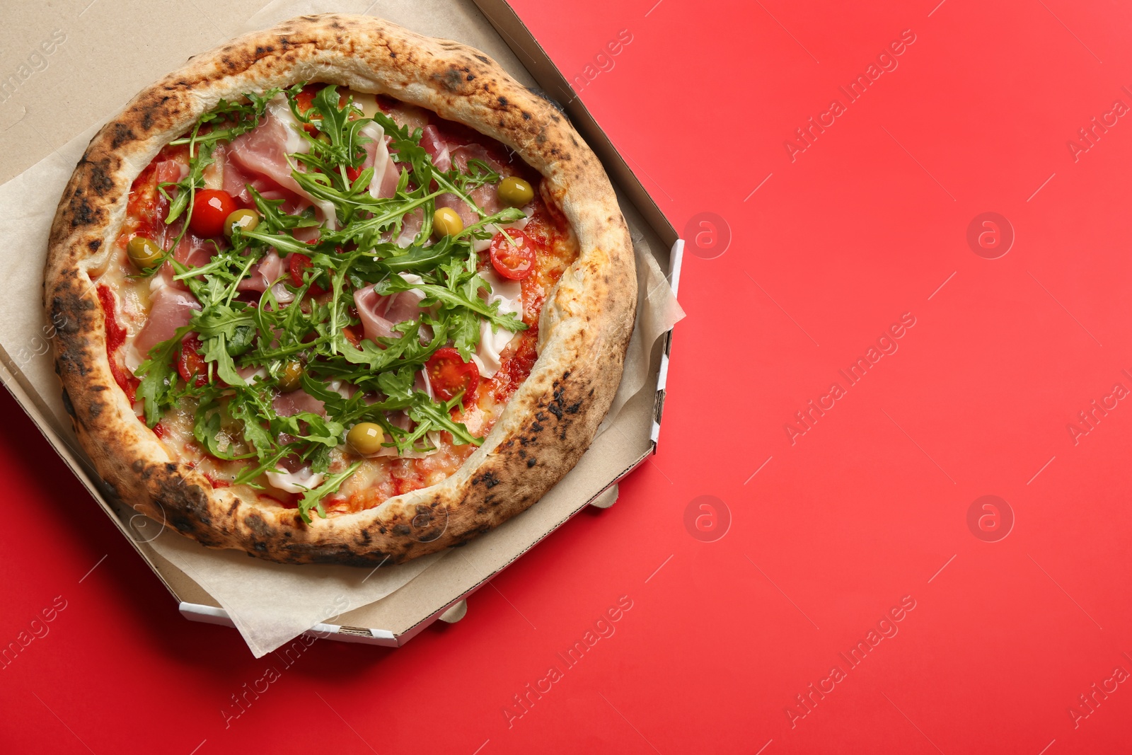Photo of Tasty pizza with meat and arugula in cardboard box on red background, top view. Space for text