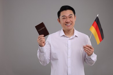 Photo of Immigration. Happy man with passport and flag of Germany on grey background, space for text