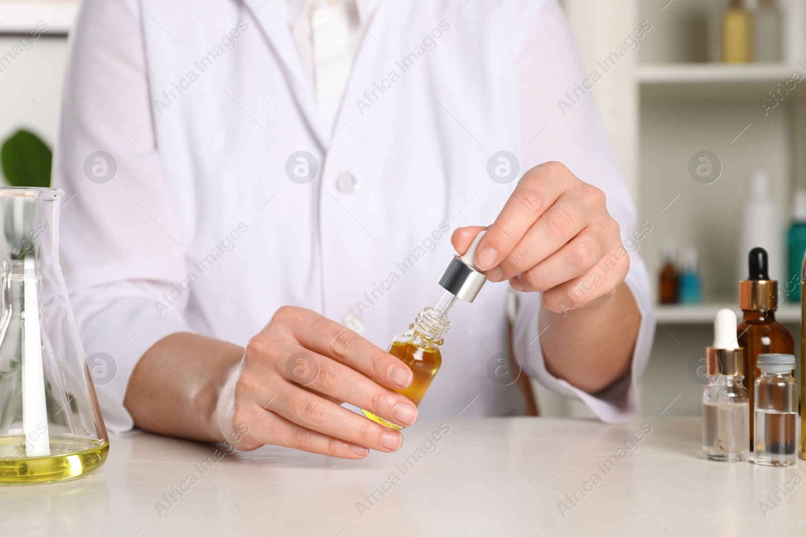 Photo of Dermatologist developing cosmetic oil at white table indoors, closeup