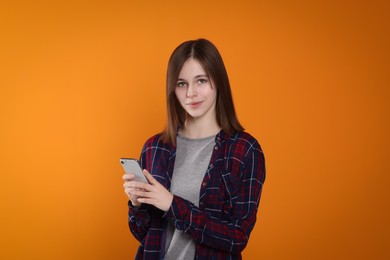 Photo of Portrait of cute teenage girl with smartphone on orange background