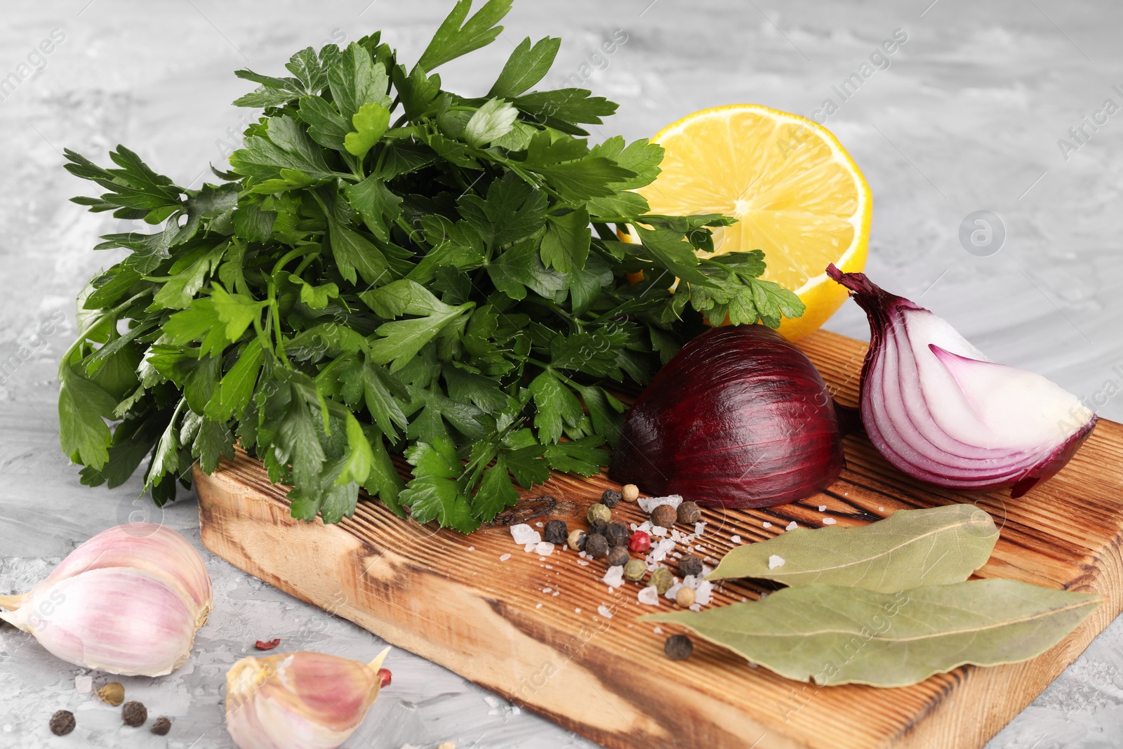 Photo of Bunch of fresh parsley, lemon, onion, garlic and spices on grey textured table