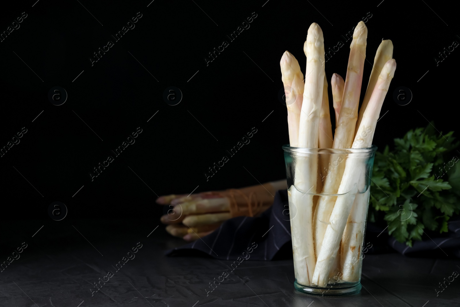 Photo of Fresh white asparagus in glass on table against black background. Space for text