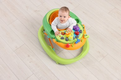 Photo of Cute baby in walker on wooden floor, above view