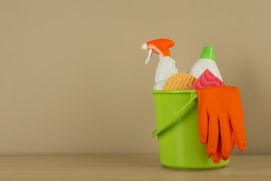 Photo of Bucket with different cleaning supplies on wooden floor near beige wall. Space for text