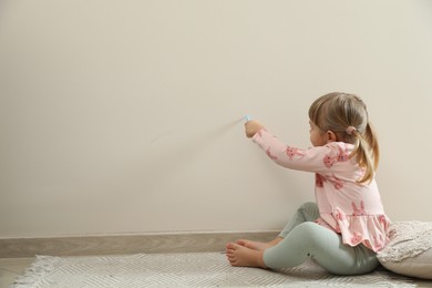 Little girl drawing on beige wall indoors, space for text. Child`s art