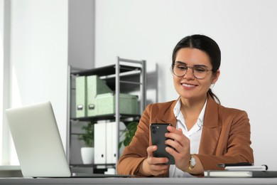 Photo of Young woman using smartphone at table in office
