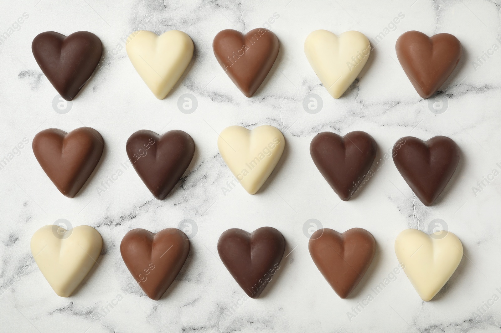 Photo of Delicious heart shaped chocolate candies on white marble table, flat lay