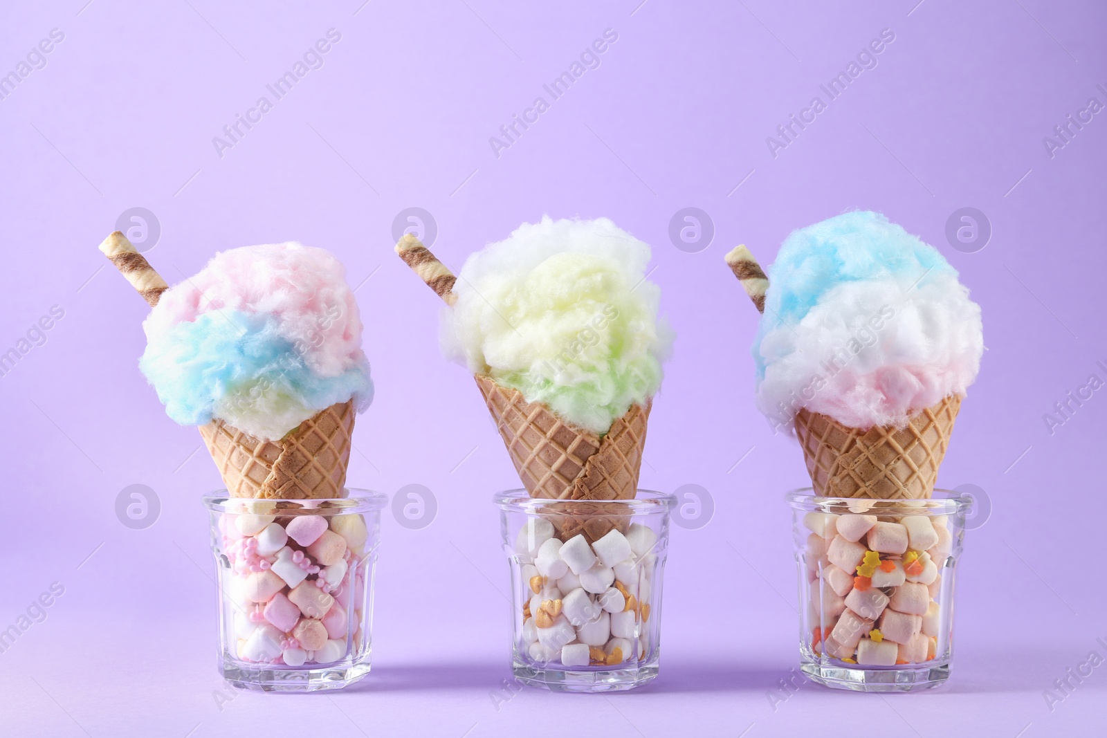 Photo of Sweet cotton candies in waffle cones on purple background, closeup