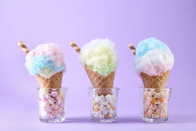 Sweet cotton candies in waffle cones on purple background, closeup