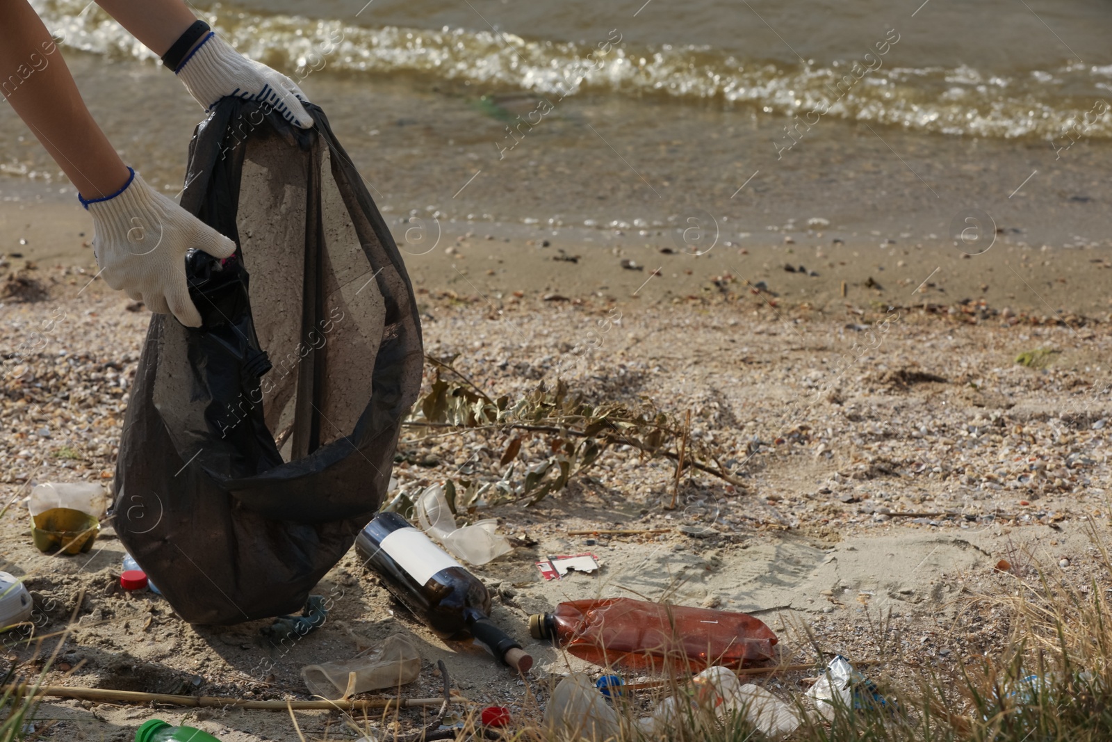 Photo of Woman in gloves with trash bag collecting garbage on beach, closeup