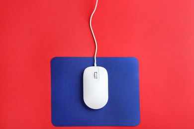Photo of Modern wired optical mouse and pad on red background, top view