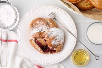 Photo of Delicious buns with sugar powder and berries on white tiled table, flat lay